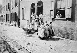 Visiting nurse entering a dilapidated row home surrounded by a group of adults and children. A yo...